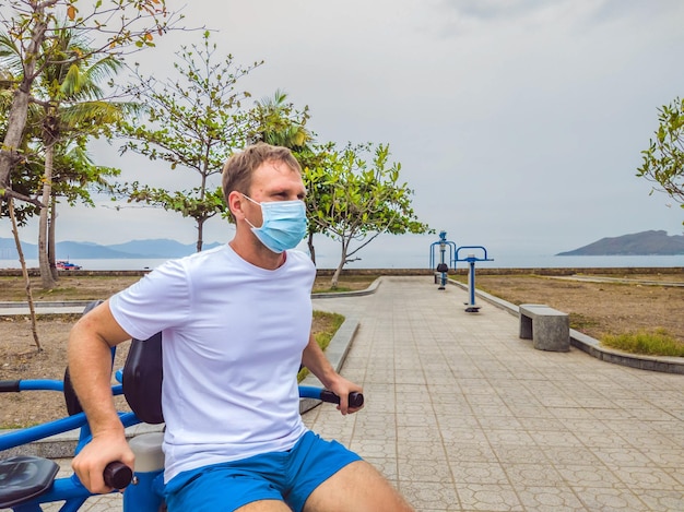 El hombre que hace ejercicios físicos empuja ejercicios de fuerza se inclina en el gimnasio de metal del parque público vacío al aire libre usando máscara solo para la prevención de Covid19 Estilo de vida saludable en cuarentena y coronavirus