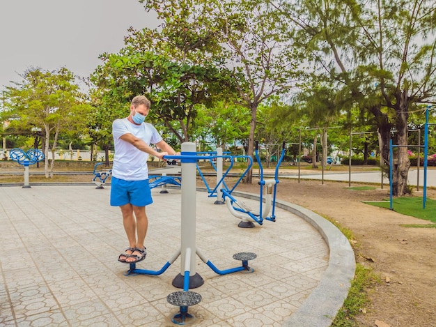 El hombre que hace ejercicios físicos empuja ejercicios de fuerza se inclina en el gimnasio de metal del parque público vacío al aire libre usando máscara solo para la prevención de Covid19 Estilo de vida saludable en cuarentena y coronavirus