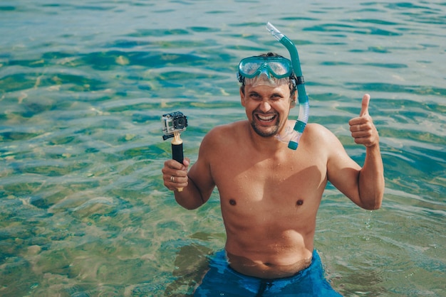 Un hombre que llevaba una máscara de buceo contra un cielo azul claro y un océano turquesa. Un buzo con una máscara de buceo con una cámara subacuática.