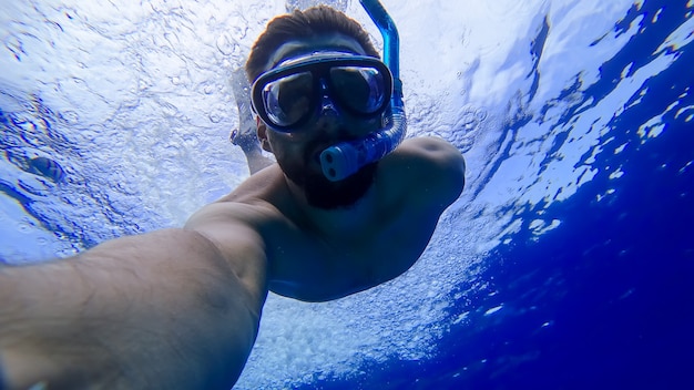 Un hombre que llevaba una máscara y un tubo de respiración se sumergió en las profundidades del mar rojo y está tratando de nadar.