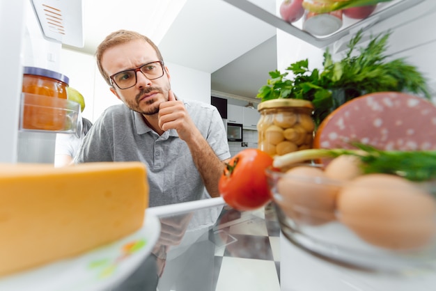 Hombre que mira dentro del refrigerador lleno de comida.