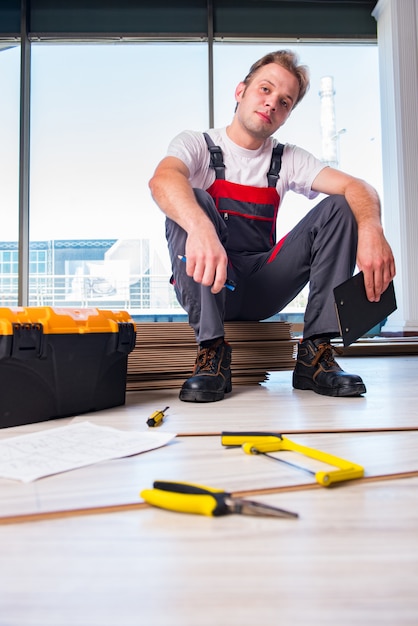 Hombre que pone el suelo laminado en concepto de la construcción