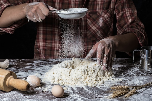 Hombre que prepara la masa de pan en la tabla de madera en un cierre de la panadería para arriba