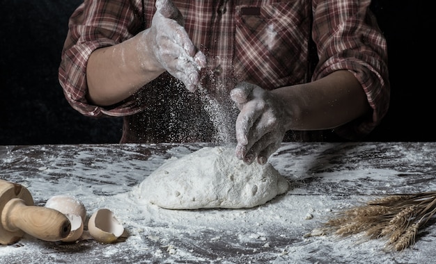 Hombre que prepara la masa de pan en la tabla de madera en un cierre de la panadería para arriba