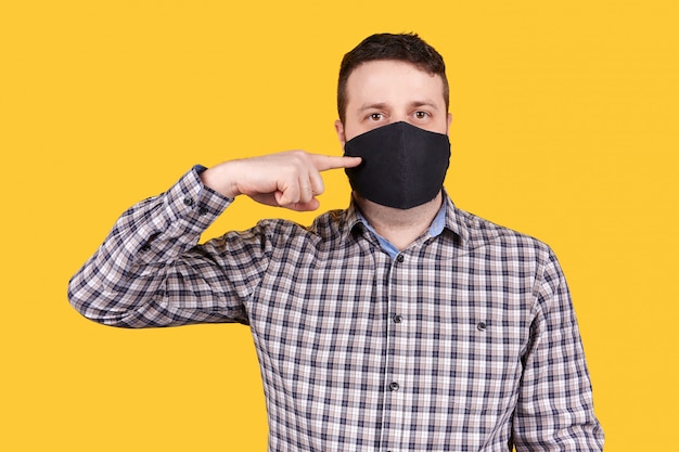 Foto hombre que señala en la mascarilla negra, aislada en espacio anaranjado.