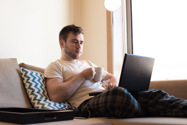 hombre que sienta, en, sofá, con, computador portatil, y, un, taza de café