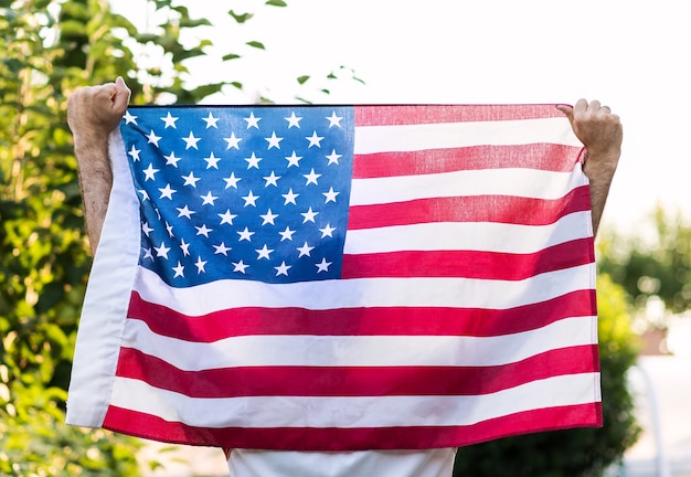 Un hombre que sostiene con ambas manos la bandera americana, para el memorial day de 4 de julio