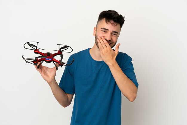 Hombre que sostiene un avión no tripulado aislado sobre fondo blanco feliz y sonriente cubriendo la boca con la mano