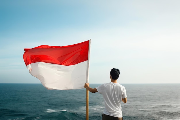 Un hombre que sostiene una bandera roja y blanca de Indonesia mirando el océano