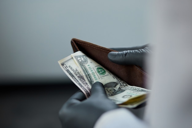 Hombre que sostiene una billetera con dólares de dinero en la mano en guantes médicos negros. Crisis del coronavirus. Ahorrar dinero. No maney