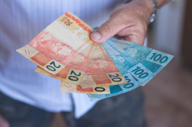 Foto hombre que sostiene los billetes de banco de dinero brasileño con sus manos.