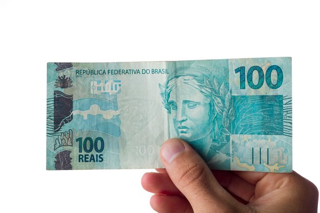 Hombre que sostiene billetes de cien reales aislados en blanco. Dinero brasileño.