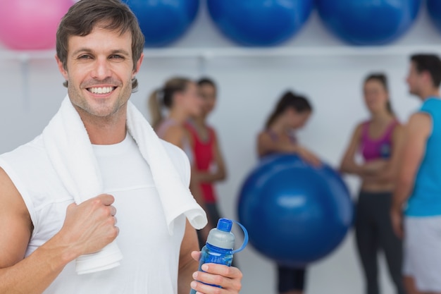 Hombre que sostiene la botella de agua con amigos en segundo plano en el gimnasio