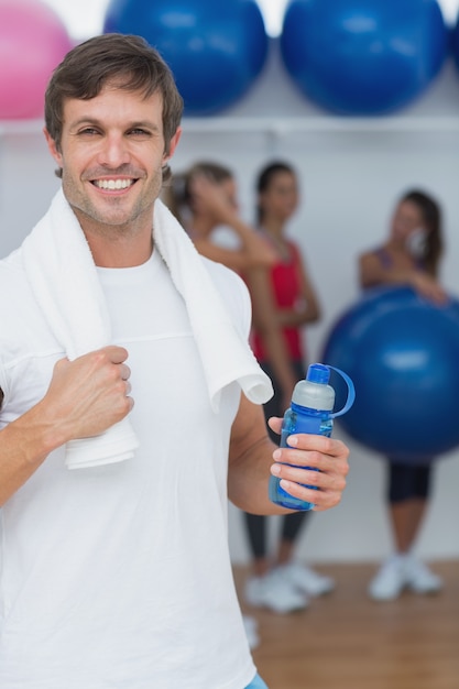 Hombre que sostiene la botella de agua con amigos en segundo plano en el gimnasio