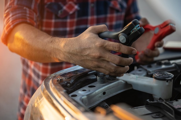 Hombre que sostiene el cable de batería rojo y negro para cargar el automóvil Concepto de mantenimiento y reparación de automóviles