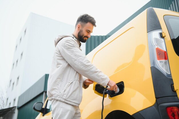 Hombre que sostiene el cable de carga de energía para el automóvil eléctrico en el estacionamiento al aire libre Y va a conectar el automóvil a la estación de carga en el estacionamiento cerca del centro comercial