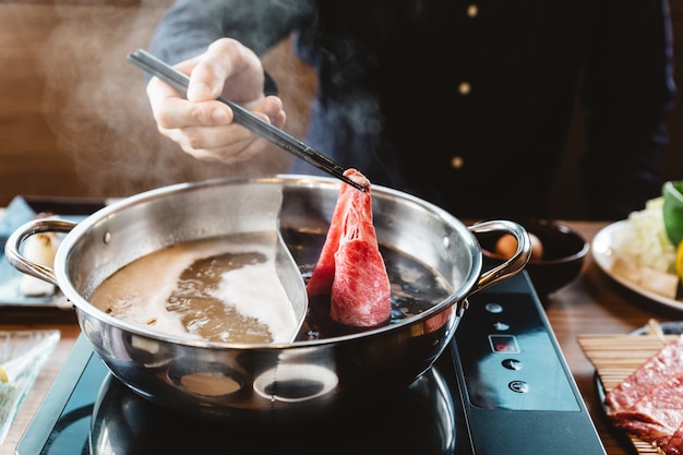 Hombre que sostiene la carne de res Wagyu A5 de la porción rara en la base de sopa shoyu shoyu de shabu con palillos