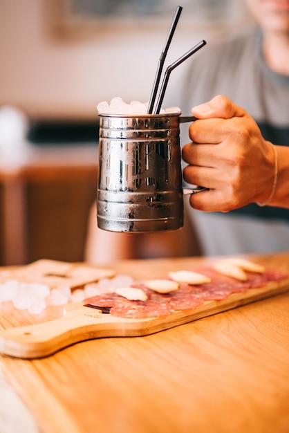 Un hombre que sostiene un cóctel de vidrio de hierro con hielo en una barra de bar y un bocadillo en primer plano