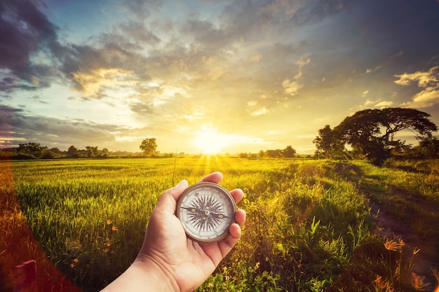 Foto un hombre que sostiene el compás en la mano en el campo y la puesta del sol para la guía de navegación.