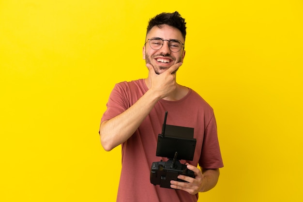 Hombre que sostiene un control remoto de drone aislado sobre fondo amarillo feliz y sonriente