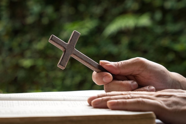 Hombre que sostiene un crucifijo cruzado religioso de madera con una biblia abierta