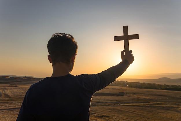 hombre que sostiene la cruz al atardecer