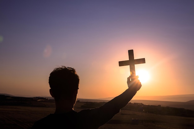 hombre que sostiene la cruz al atardecer