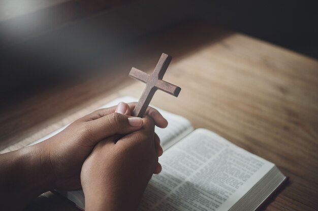 Hombre que sostiene la cruz de madera en las manos sobre la Biblia y la luz divina. Concepto de religión.