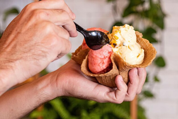 Un hombre que sostiene una cucharada de helado con una planta verde detrás de él.