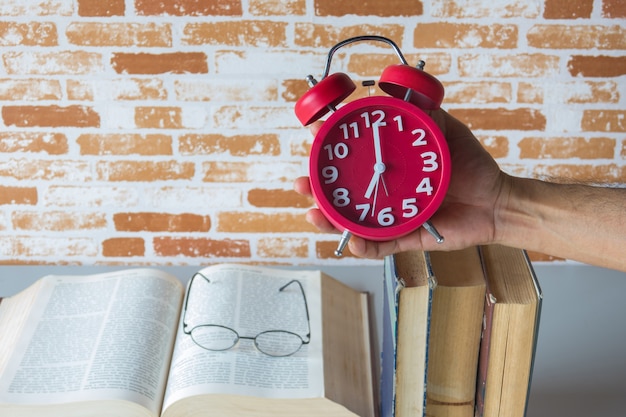 Foto un hombre que sostiene el despertador por encima de libros abiertos, tiempo de lectura