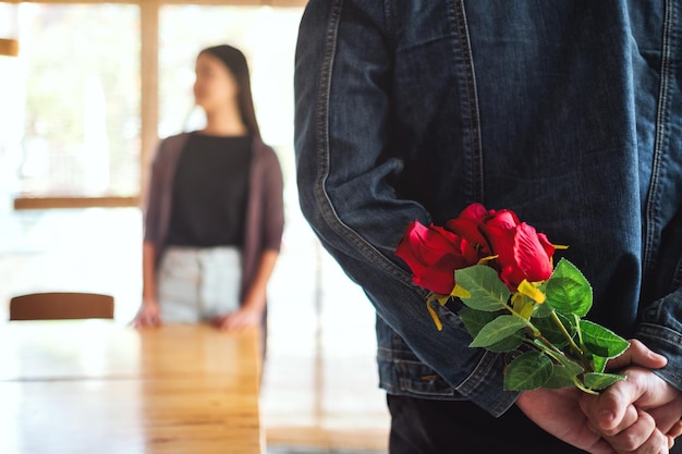 Un hombre que sostiene y esconde el ramo de rosas rojas en la espalda para sorprender a la novia