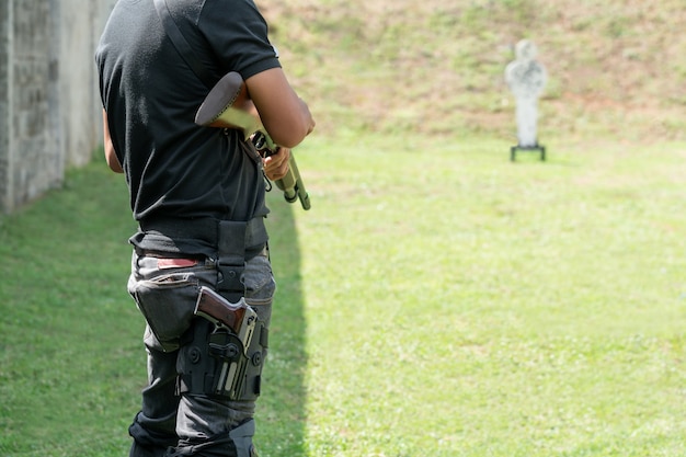 Foto el hombre que sostiene la escopeta y lleva la pistola en la pantorrilla al frente de target en el campo de tiro.