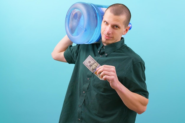 Foto hombre que sostiene un galón de agua en el hombro y muestra 100 dólares en la mano sobre un fondo azul entrega de agua galón hogar hombre botella pagar paga ganancias dólar etiqueta blanca