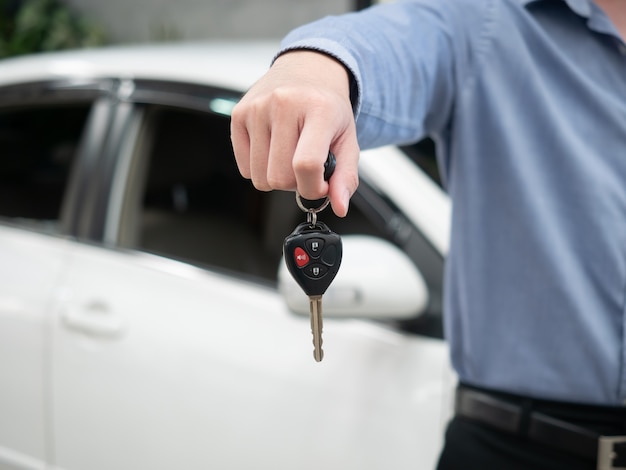 Hombre que sostiene la llave en concesionario de automóviles moderno. Cerrar la mano de cardealer dando la llave del auto al cliente