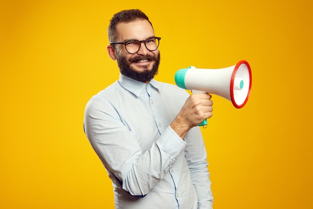 Hombre que sostiene el megáfono y sonriendo mientras está de pie aislado sobre amarillo