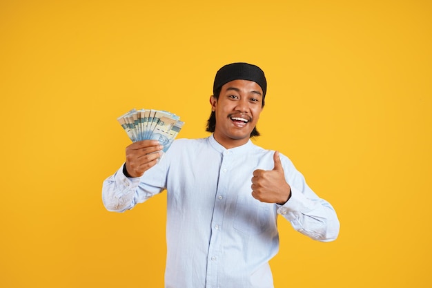 Un hombre que sostiene una pila de dinero con los pulgares hacia arriba.