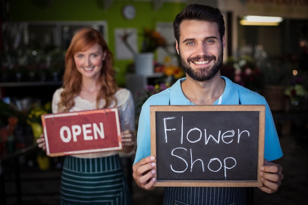 Hombre que sostiene la pizarra con el cartel de la tienda de flores y la mujer que sostiene el letrero abierto