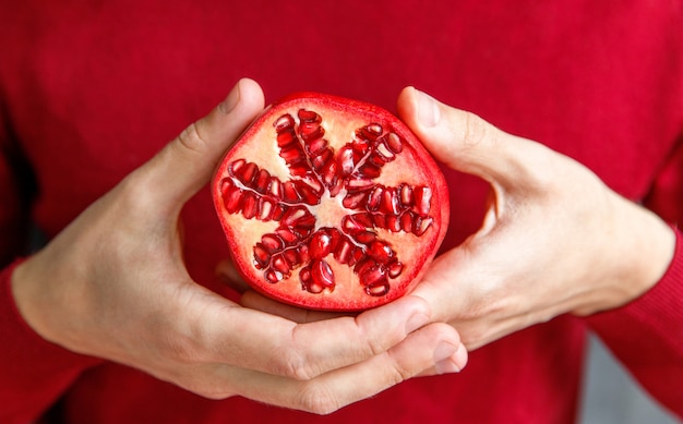 Hombre que sostiene y que muestra la granada madura cortada. Las frutas de granada son ricas en azúcares, taninos, vitamina C