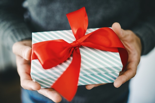 Hombre que sostiene el regalo con cinta roja