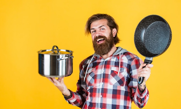 Hombre que sostiene la sartén. Chef masculino cocinando. Camisa hipster para cocinero barbudo. hombre brutal sin afeitar con utensilio de cocina. artículos de uso doméstico. asistente de tienda amigable. Trae la fiesta de comida.