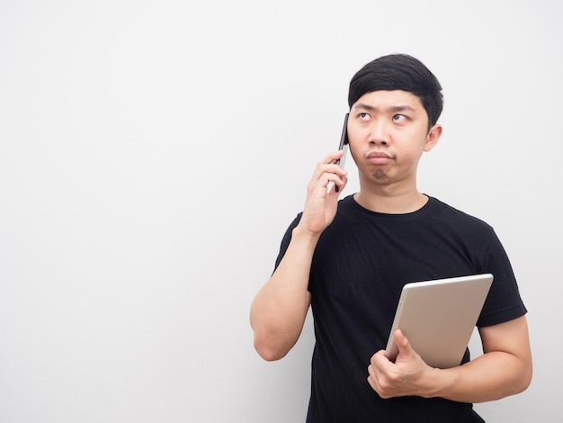 Hombre que sostiene la tableta hablando con el teléfono móvil sintiéndose aburrido mirando el espacio de la copia