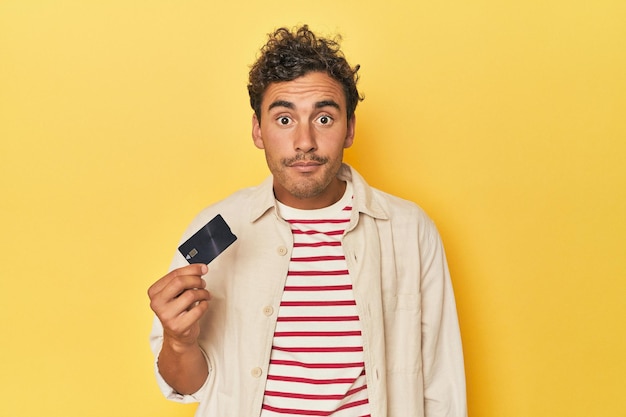 El hombre que sostiene la tarjeta de crédito en amarillo se encoge de hombros y abre los ojos confundido