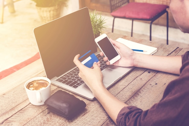 Hombre que sostiene la tarjeta de crédito y que usa la computadora portátil y el smartphone. Pago en línea.