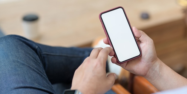 hombre que sostiene el teléfono inteligente de pantalla en blanco mientras está sentado en un lugar de trabajo cómodo