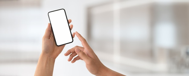 Foto un hombre que sostiene el teléfono inteligente de pantalla en blanco en la oficina borrosa