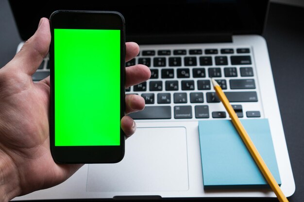 Hombre que sostiene el teléfono inteligente con pantalla de clave de croma verde en el lugar de trabajo moderno de fondo