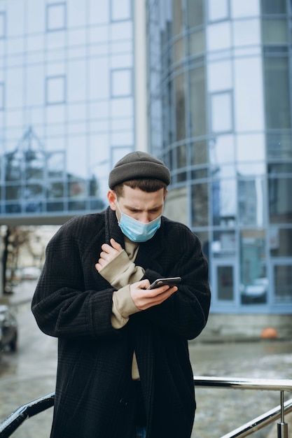 Un hombre que sostiene un teléfono inteligente y usa una máscara protectora contra enfermedades infecciosas transmisibles y como protección contra la contaminación y la gripe.