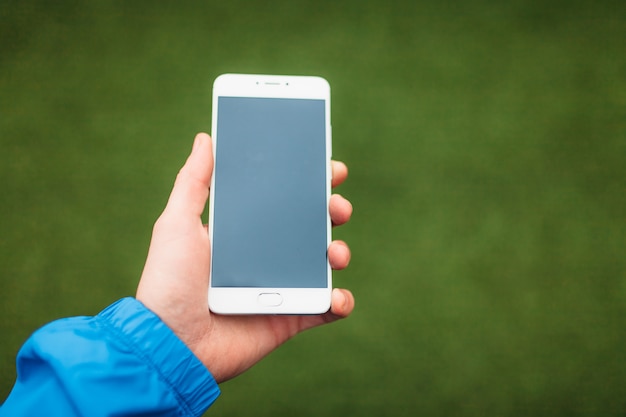 Hombre que sostiene el teléfono en la mano, sobre un fondo de campo de fútbol verde.