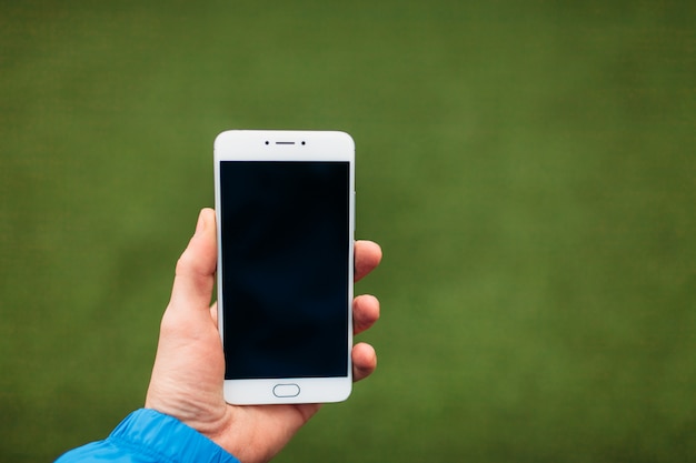 Foto hombre que sostiene el teléfono en la mano, sobre un fondo de campo de fútbol verde.