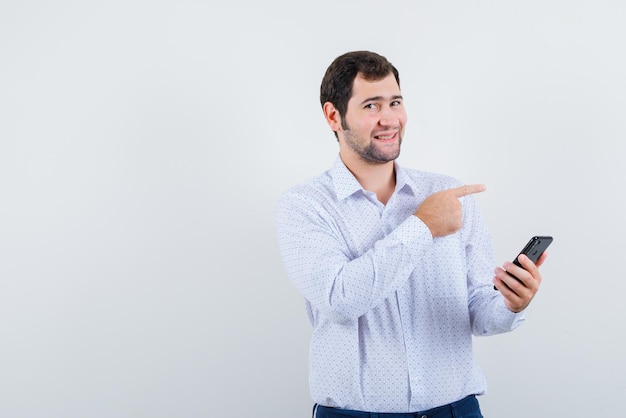 El hombre que sostiene el teléfono móvil está apuntando a la derecha con el dedo índice sobre fondo blanco.